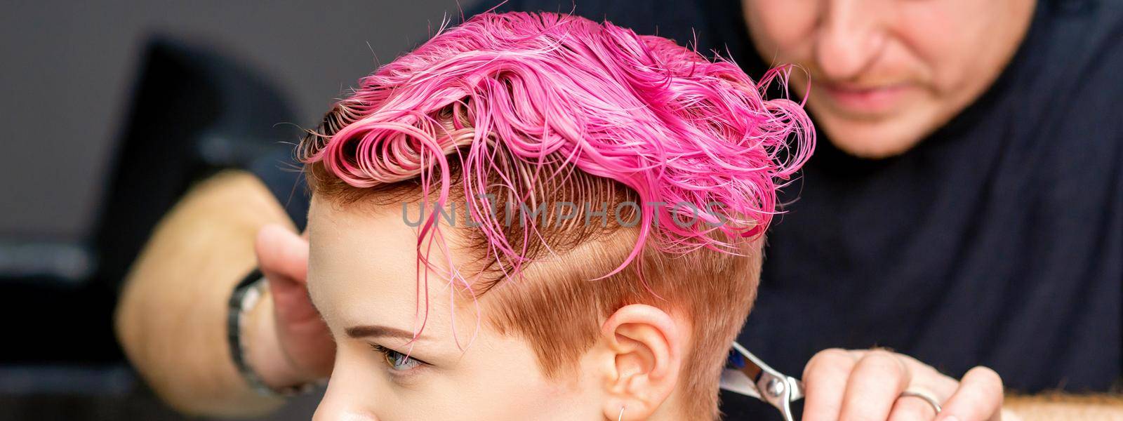 Woman having a new haircut. A male hairstylist is cutting dyed pink short hair with scissors in a hair salon. by okskukuruza