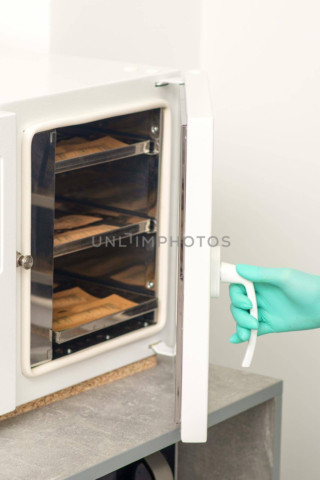 Beautician in protective gloves close the door of the machine for disinfection of tools before the depilation procedure