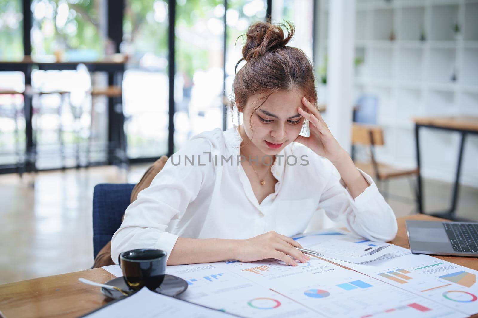 A portrait of a young employee showing an anxious and stressed face from working on paperwork on a desk.