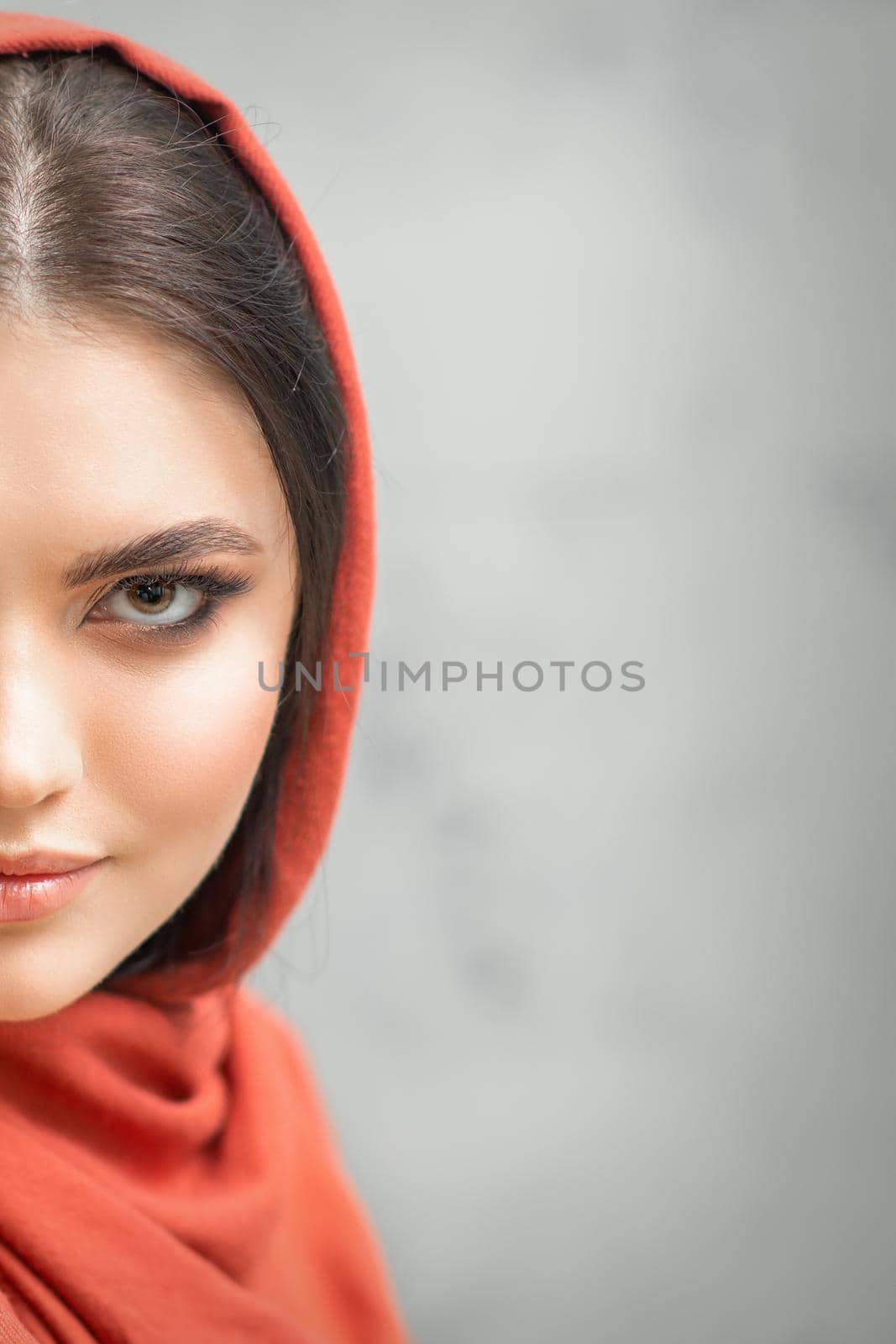 Portrait of a pretty young caucasian woman with makeup in a red headscarf on gray background