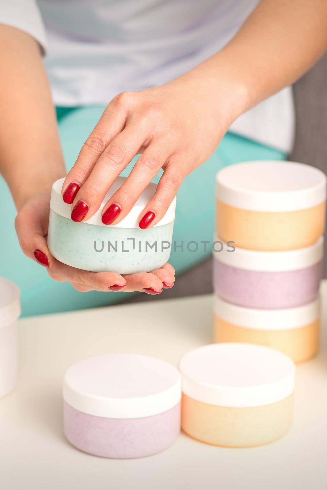 Female hands open a white body cream jar over the table with many jars of cosmetics