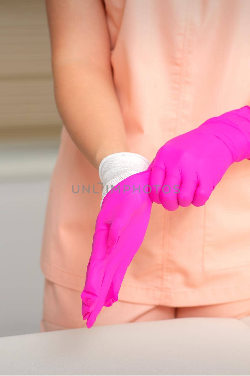 Hand of beautician puts on sterile pink gloves prepares to receive clients indoors. by okskukuruza