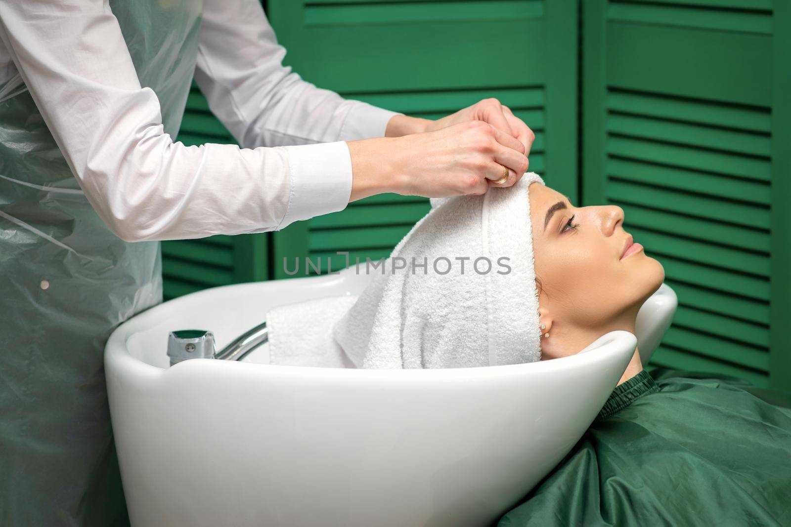 A hairdresser is wrapping a female head in a towel after washing hair in the beauty salon