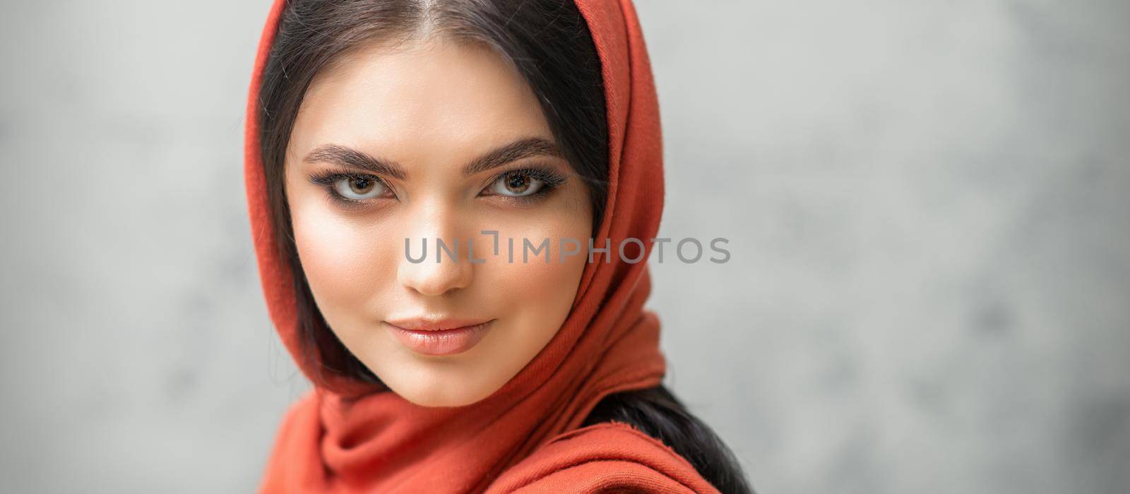 Portrait of a pretty young caucasian woman with makeup in a red headscarf on gray background. by okskukuruza