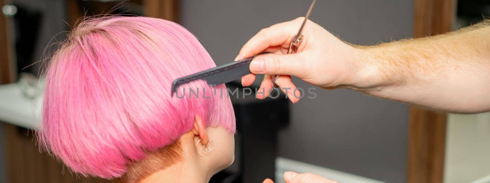 Hands of hairdresser combing hair making short pink hairstyle for a young caucasian woman in a beauty salon. by okskukuruza