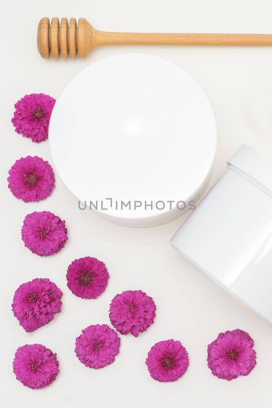Flat lay composition of white jars with flowers on white background, skincare cosmetics, top view