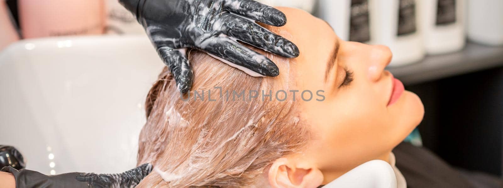 Young caucasian blonde woman having hair washed in the sink at a beauty salon. by okskukuruza