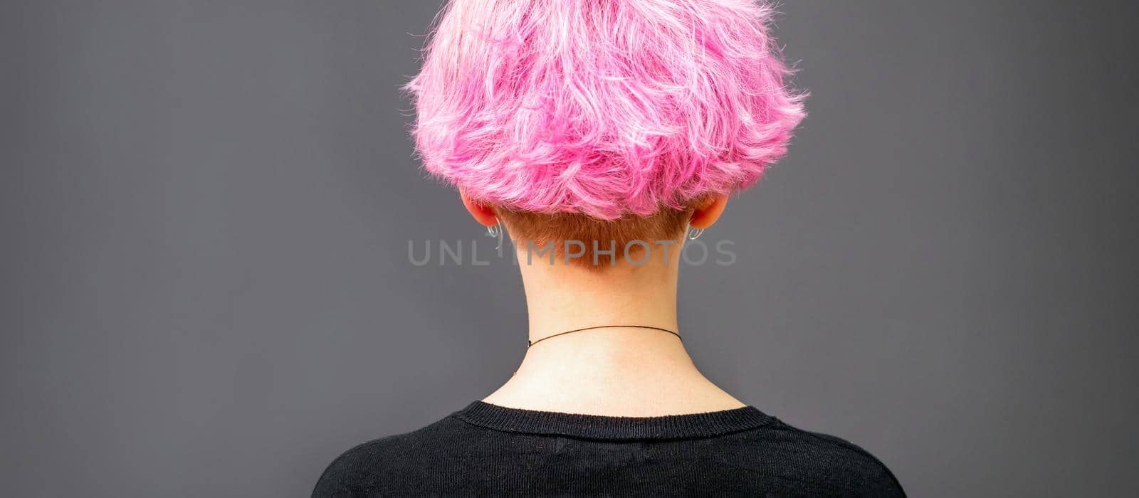 Back of female head with curly short pink hair against the dark background