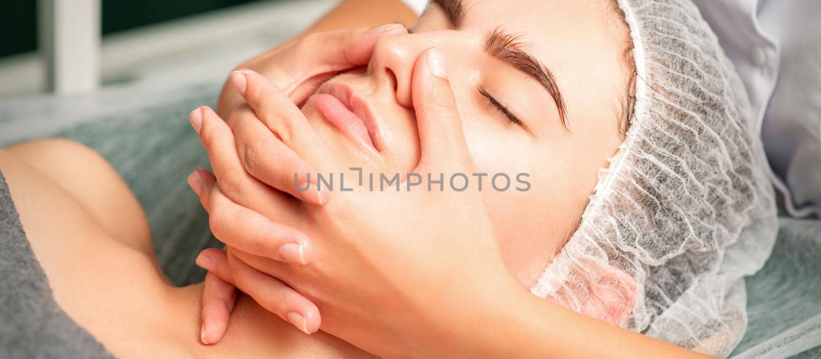 A young caucasian woman getting facial massage in a spa. by okskukuruza