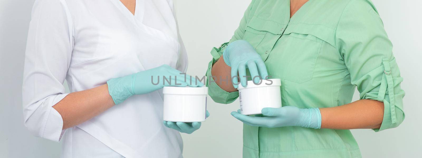 Two cosmeticians with jars of wax for depilation smiling against a white background. Natural product for hair removal. Copy space