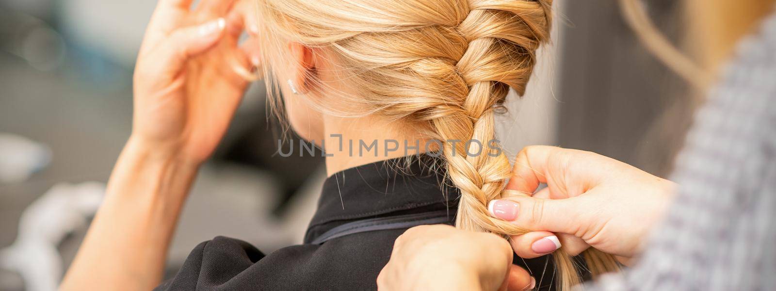 Braiding braid. Hands of female hairdresser braids long braid for a blonde woman in a hair salon