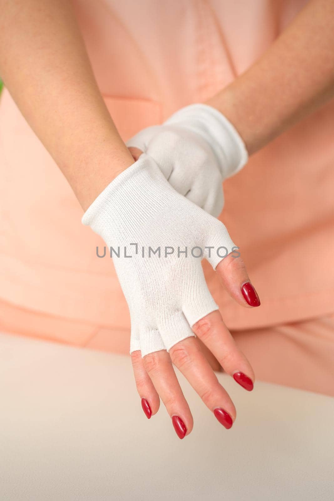 Cosmetician in workwear wearing white bamboo fingerless gloves on her hands in a beauty salon. by okskukuruza