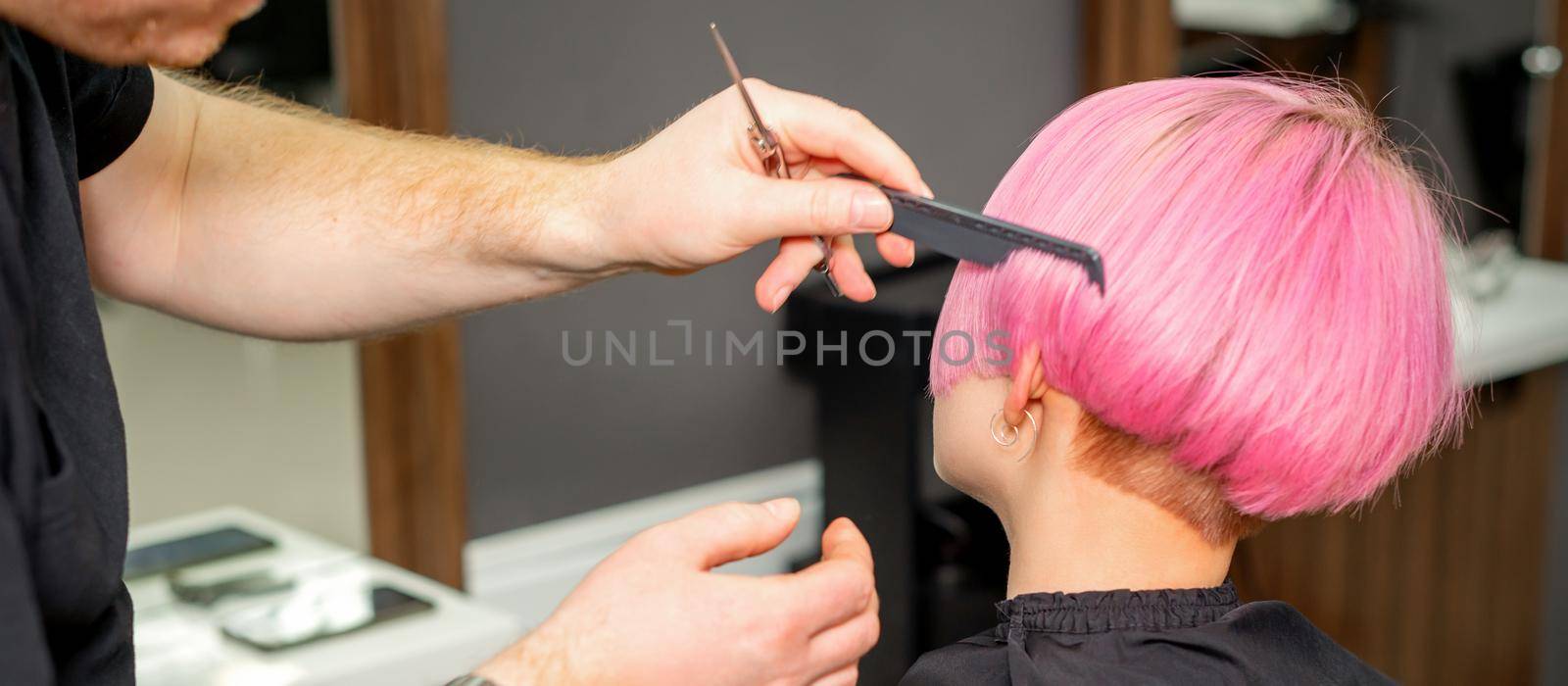 Hands of hairdresser combing hair making short pink hairstyle for a young caucasian woman in a beauty salon. by okskukuruza