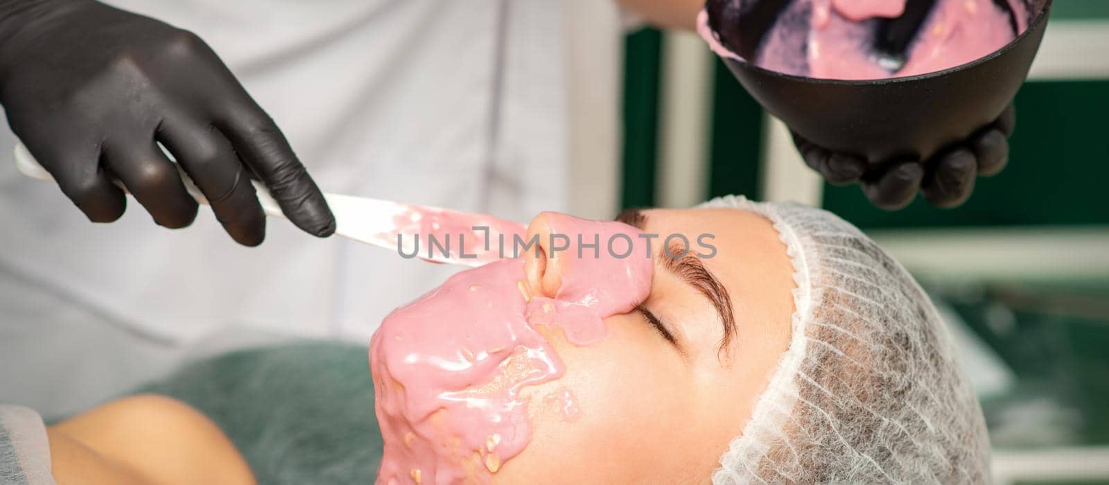 The cosmetologist applying an alginate mask to the face of a young woman in a beauty salon. by okskukuruza