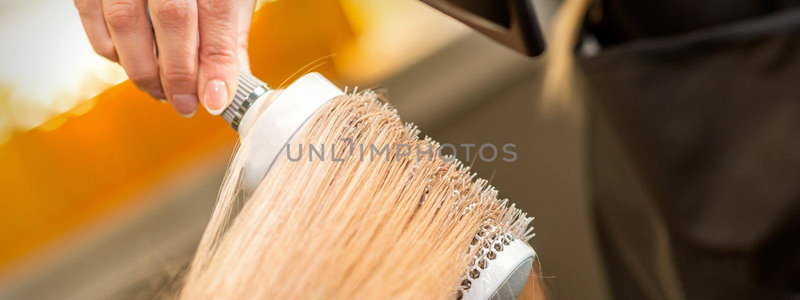 Hairdresser hand drying blond hair with a hairdryer and round brush in a beauty salon