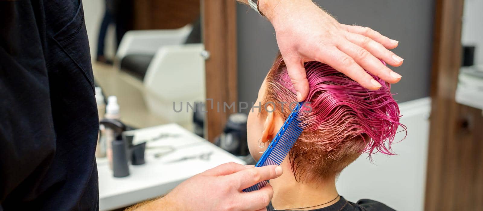 Hands of hairdresser combing hair making short pink hairstyle for a young caucasian woman in a beauty salon