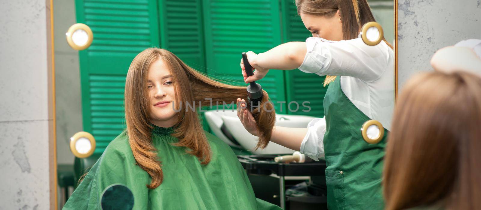 Hairdresser making hairstyling for the woman while combing with hairbrush, comb in a hair salon