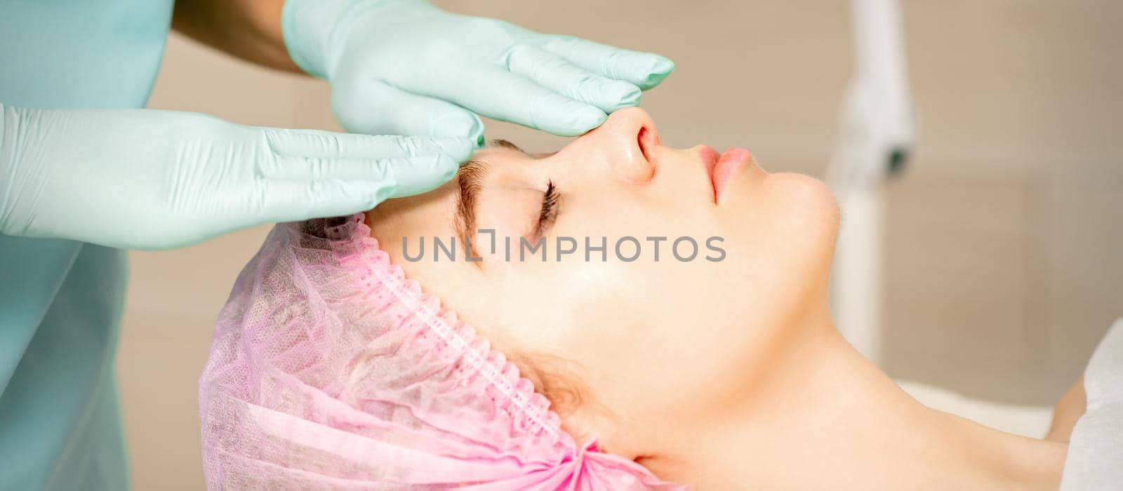 Face peeling at the beautician. Facial treatment. The beautician applies a cleansing face mask to the female patient. by okskukuruza