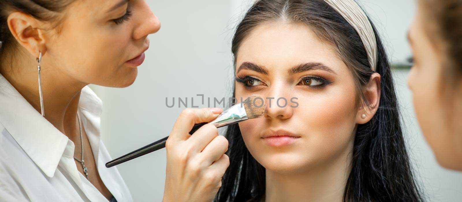 Closeup portrait of a woman applying dry cosmetic tonal foundation on the face using a makeup brush. Makeup detail