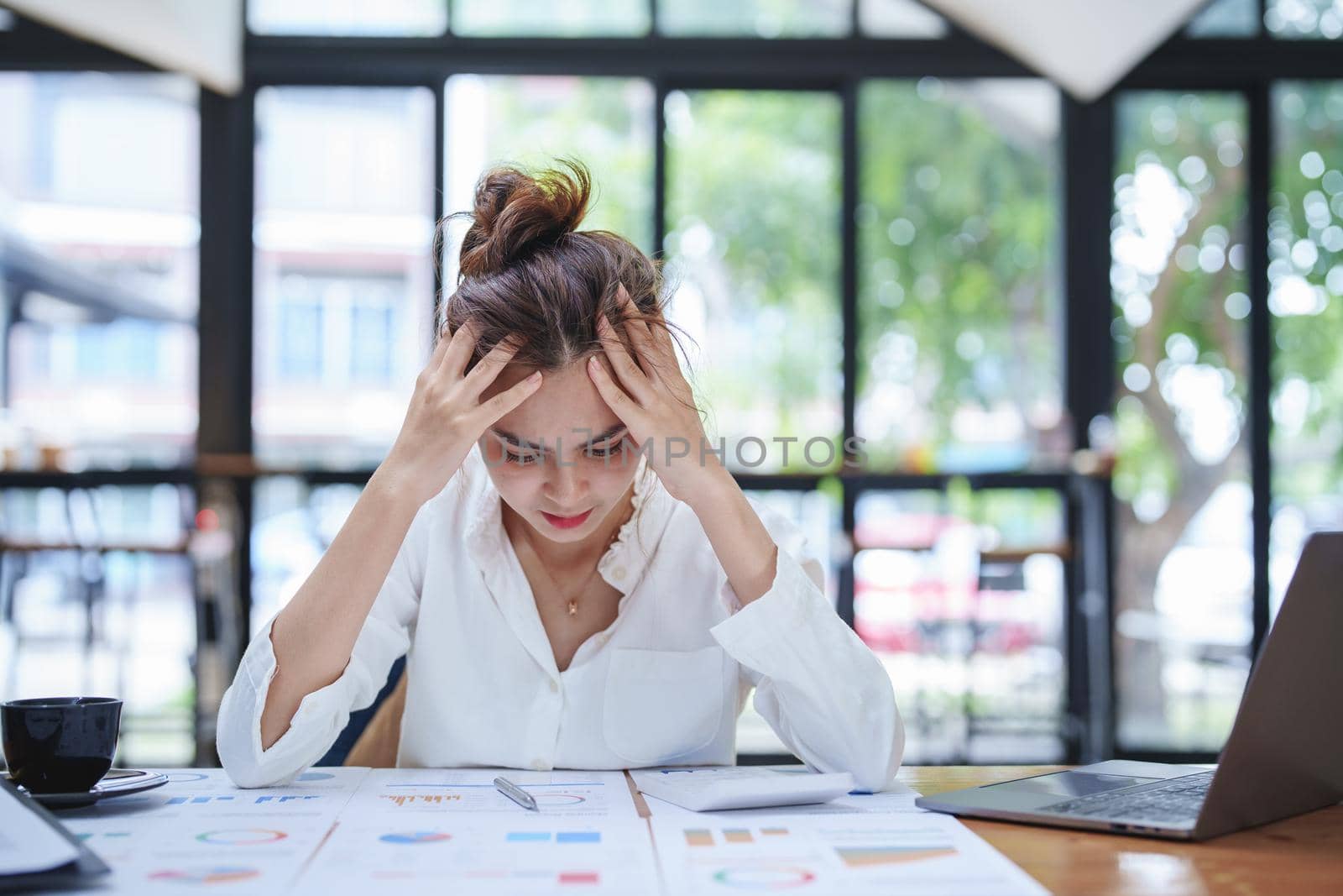 A portrait of a young employee showing an anxious and stressed face from working on paperwork on a desk.