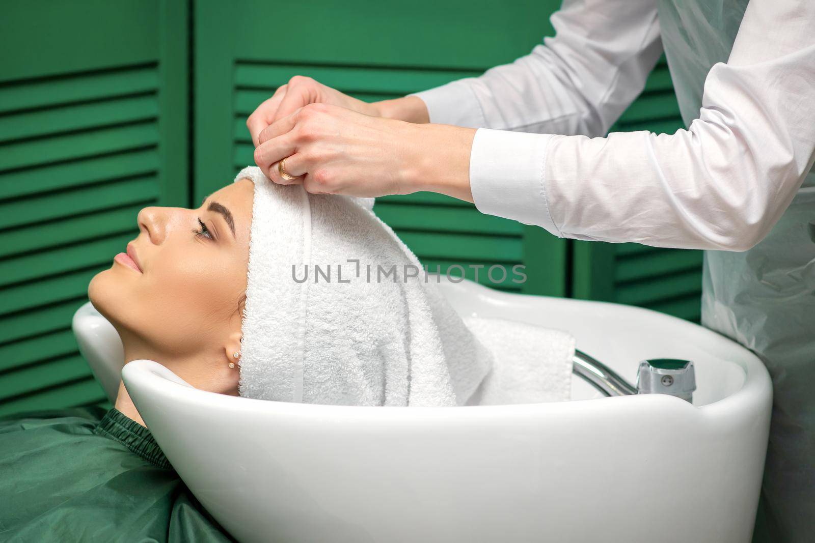 A hairdresser is wrapping a female head in a towel after washing hair in the beauty salon