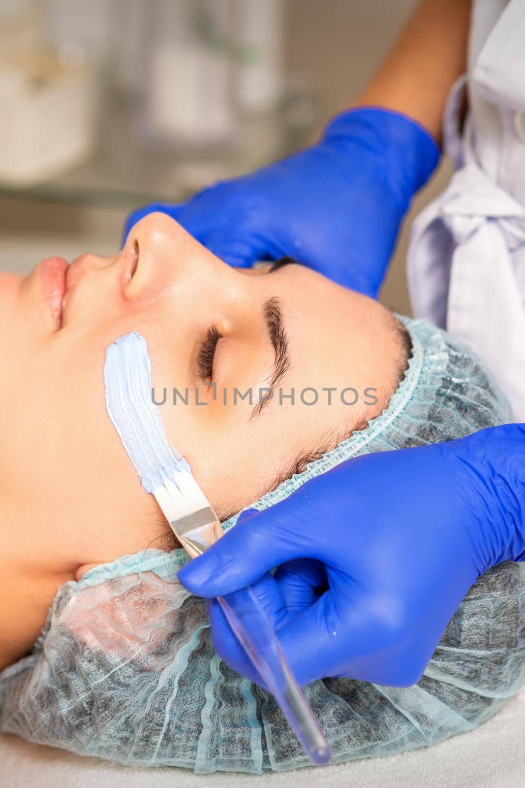 Face peeling at the beautician. Facial treatment. The beautician applies a cleansing face mask to the female patient