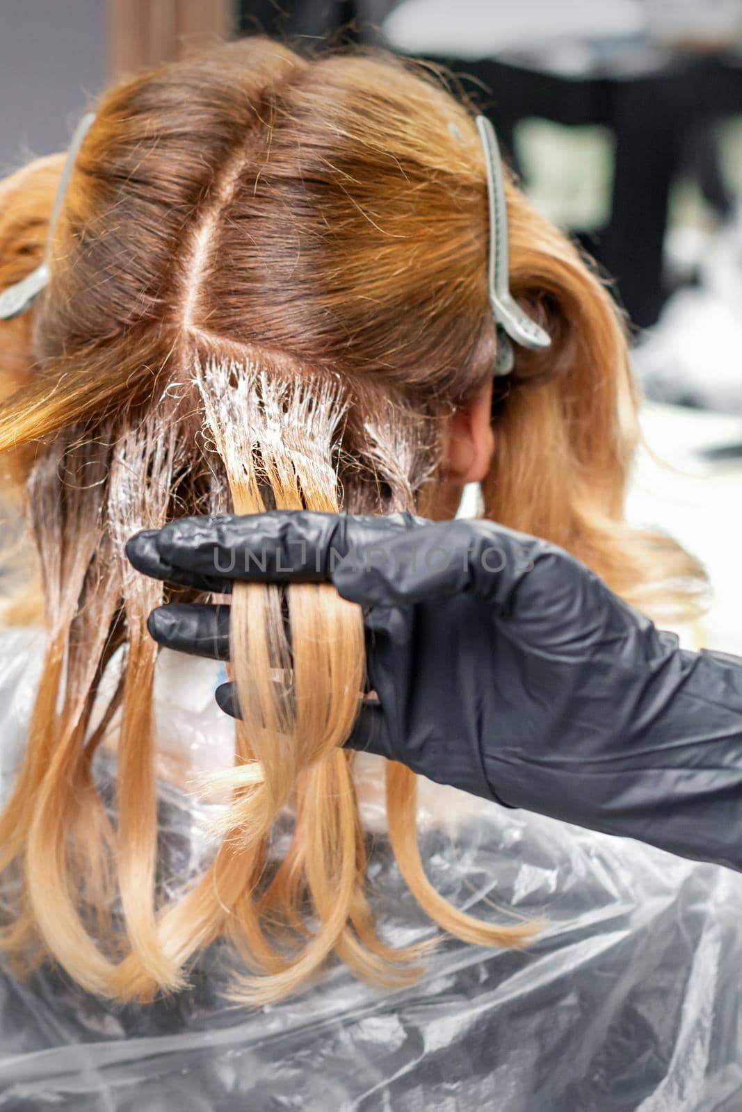 A hairdresser is applying color to hair in black gloves. Hair coloring in a beauty salon. Beauty concept. by okskukuruza