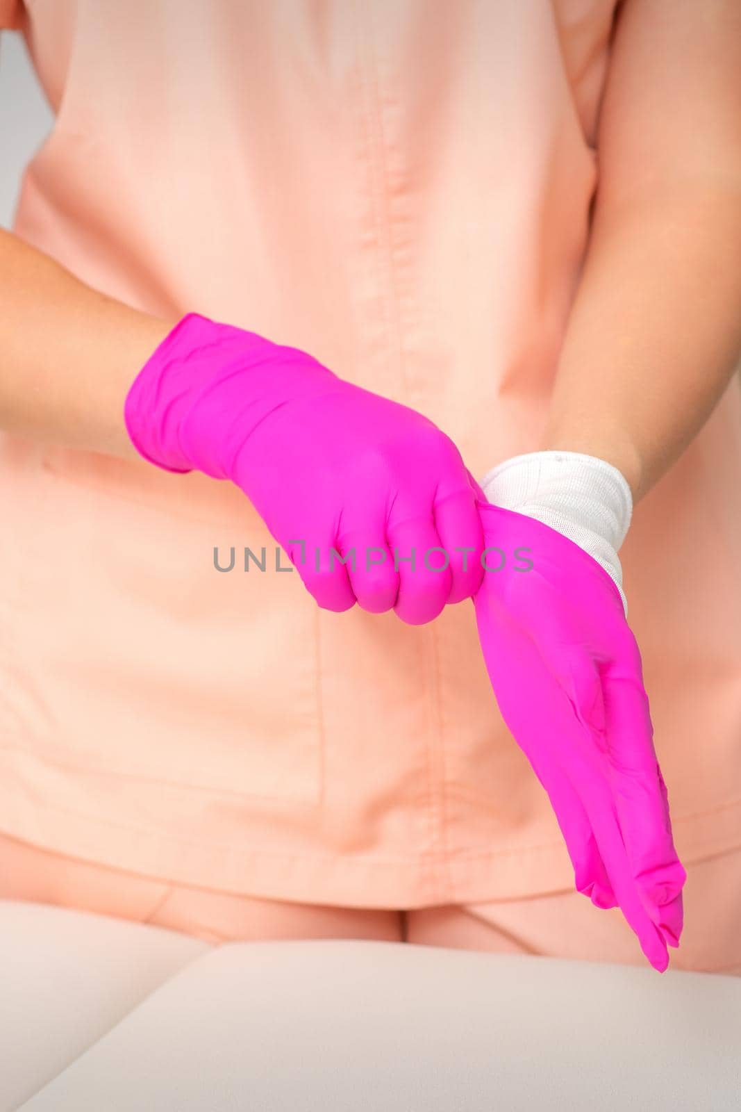 Hand of beautician puts on sterile pink gloves prepares to receive clients indoors. by okskukuruza