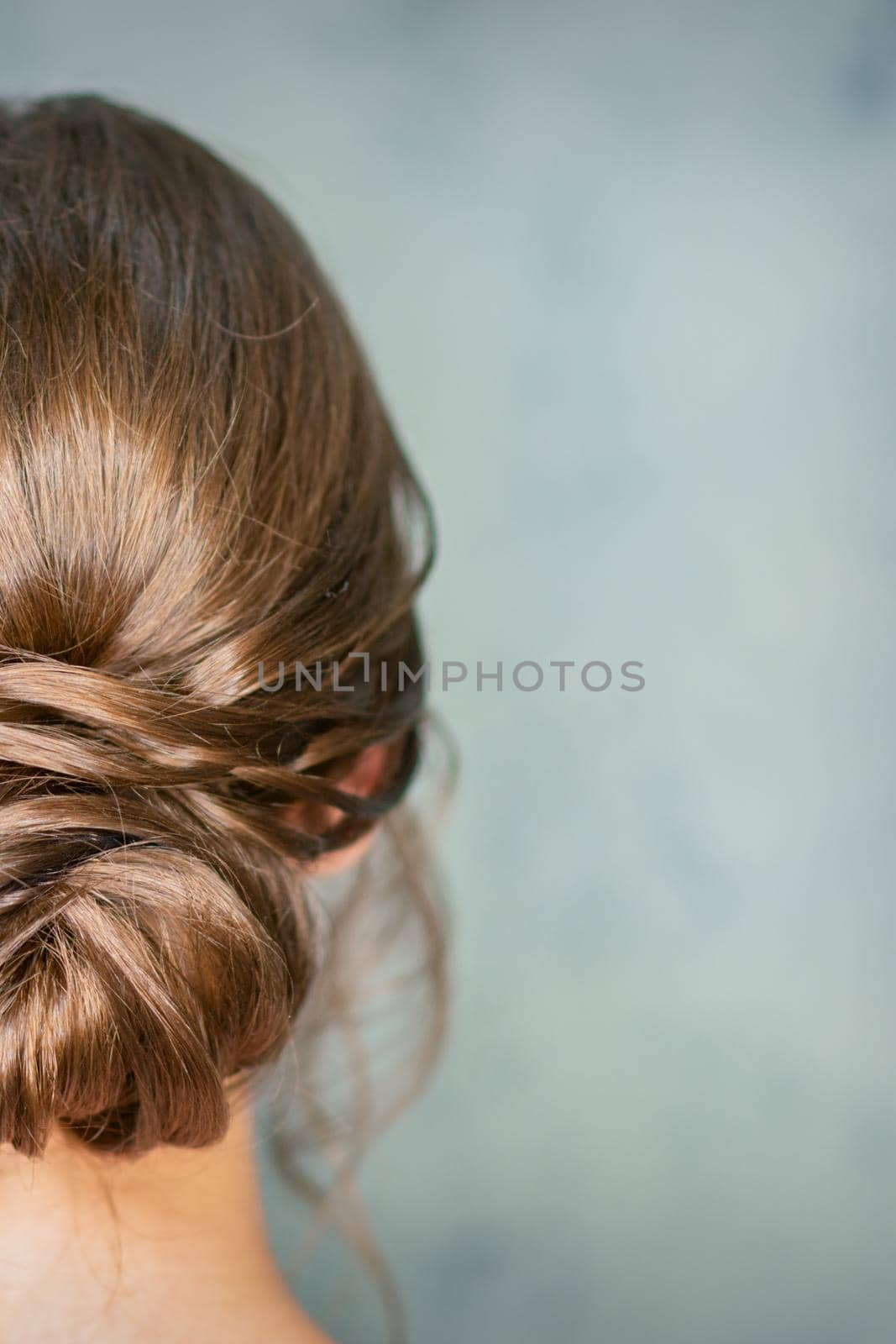Rearview of young brunette woman with beautiful middle bun hairstyle on gray background. by okskukuruza