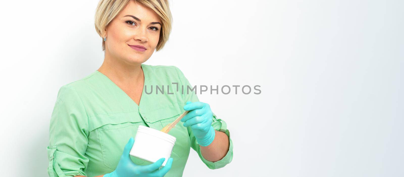 Cosmetician holding a jar of wax for depilation smiling on a white background. Natural product for hair removal. Copy space. by okskukuruza