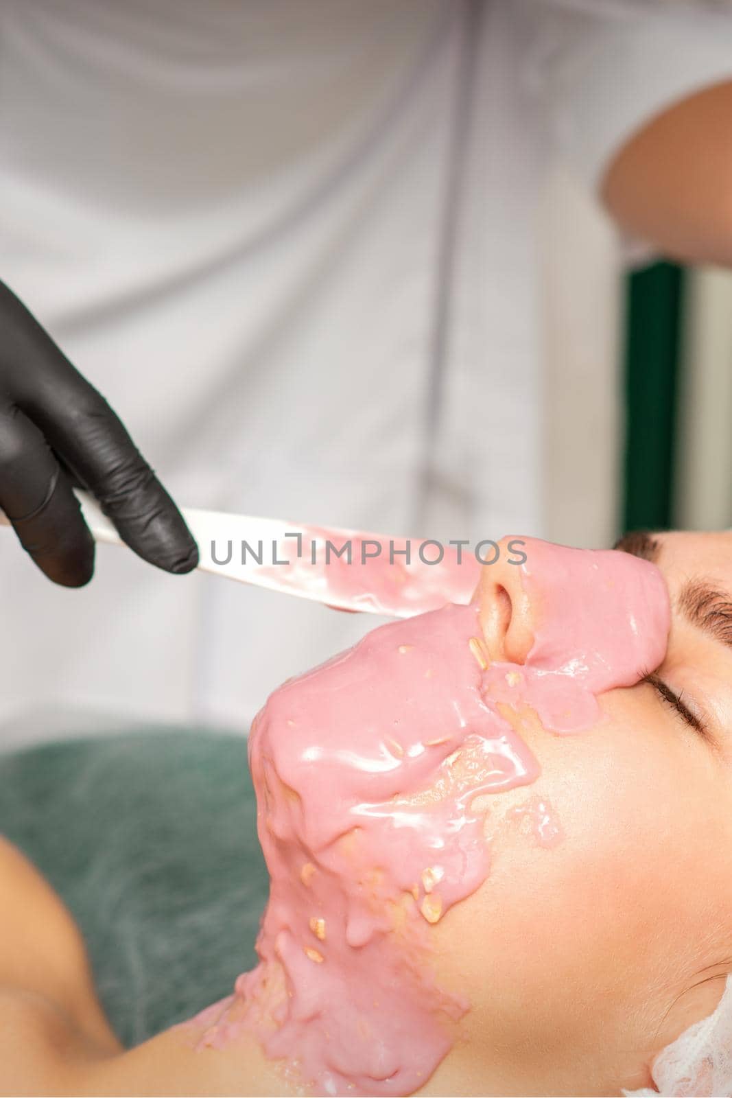 The cosmetologist applying an alginate mask to the face of a young woman in a beauty salon