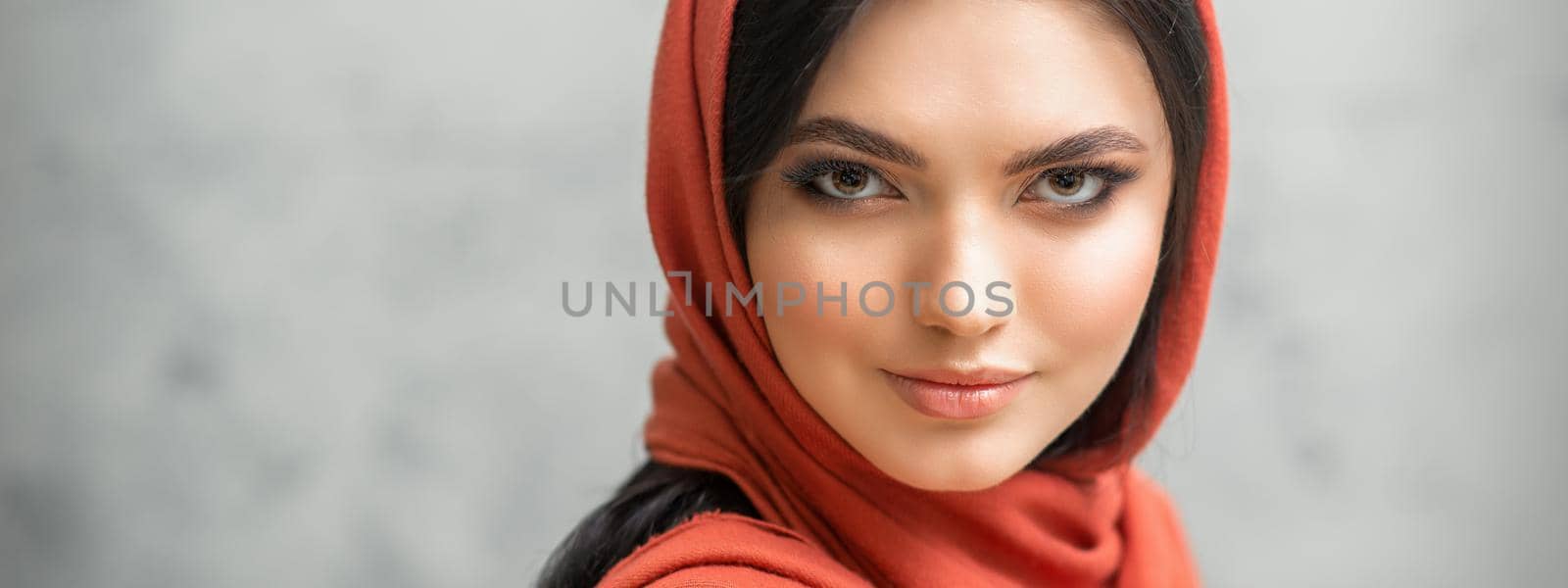 Portrait of a pretty young caucasian woman with makeup in a red headscarf on gray background