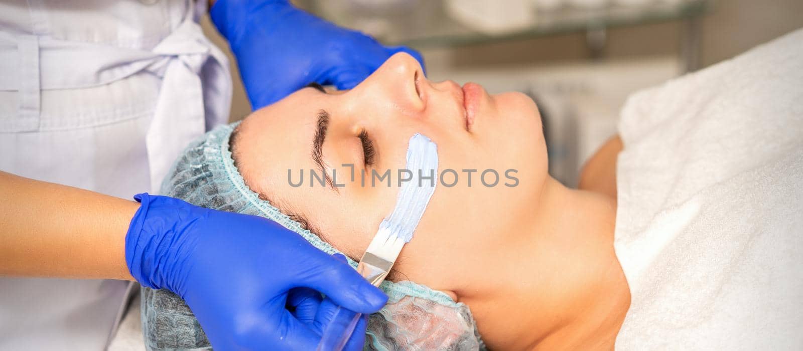 Face peeling at the beautician. Facial treatment. The beautician applies a cleansing face mask to the female patient