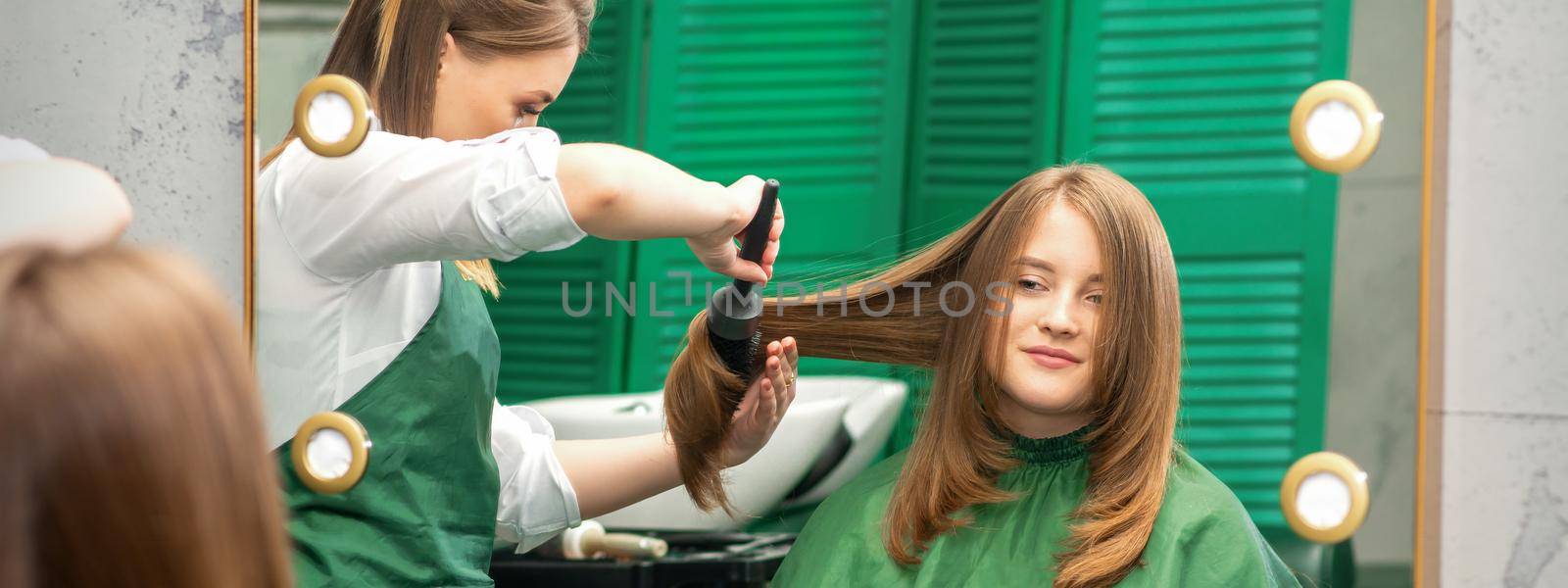 Hairdresser making hairstyling for the woman while combing with hairbrush, comb in a hair salon