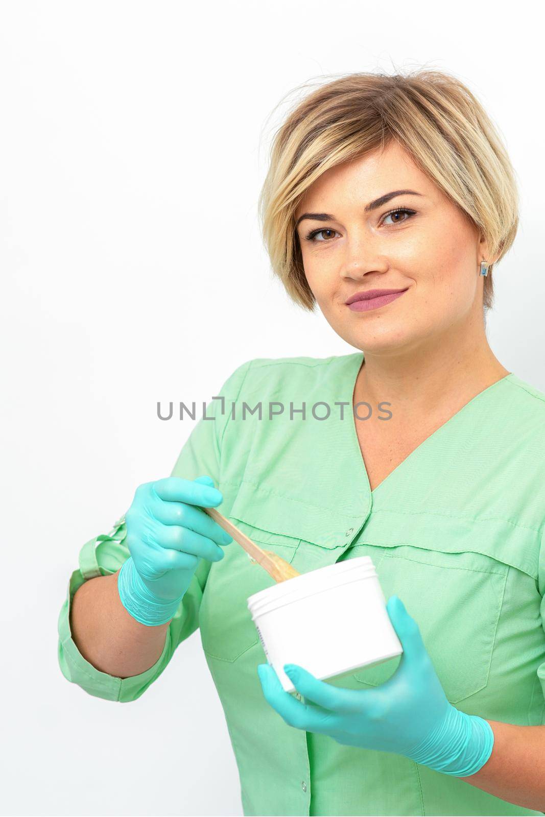 Cosmetician holding a jar of wax for depilation smiling on a white background. Natural product for hair removal. Copy space. by okskukuruza