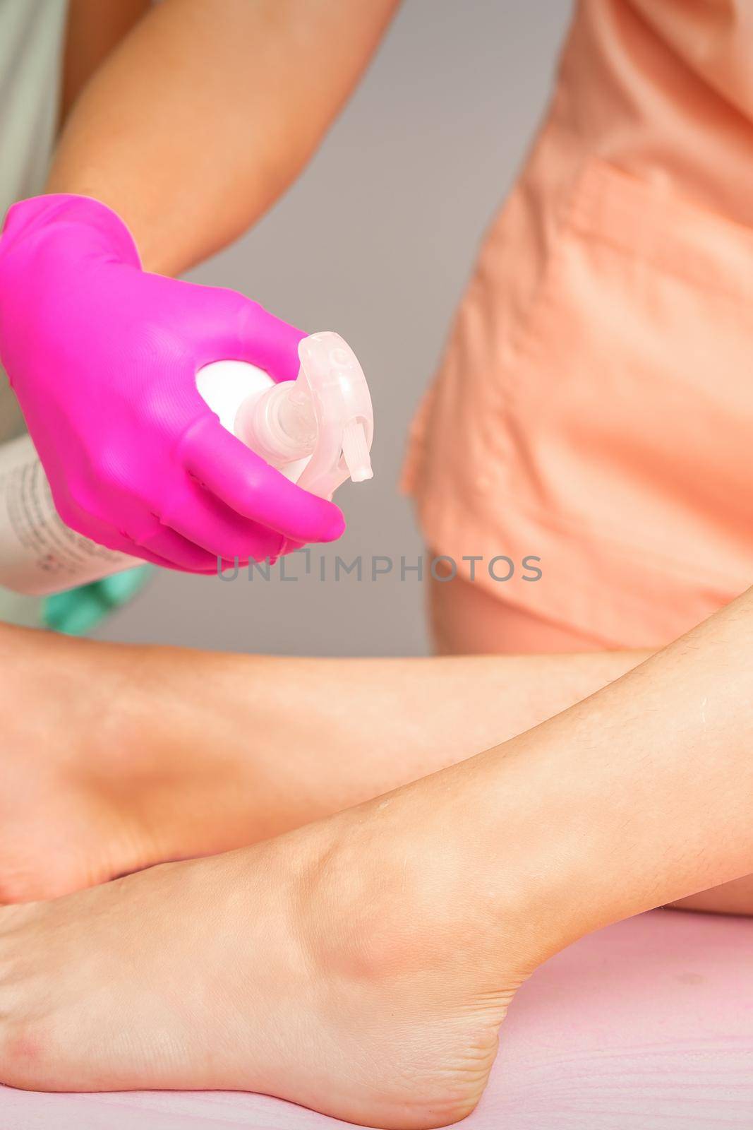 A beautician sprays a disinfectant on the feet of a young woman before the epilation procedure. Foot depilation. by okskukuruza