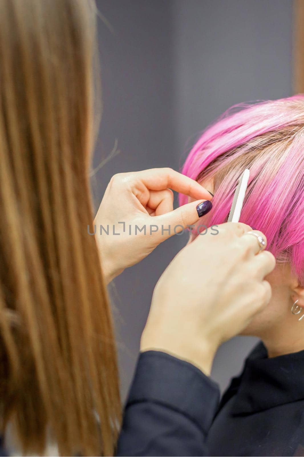 Hairdresser prepares dyed short pink hair of a young woman to procedures in a beauty salon. by okskukuruza