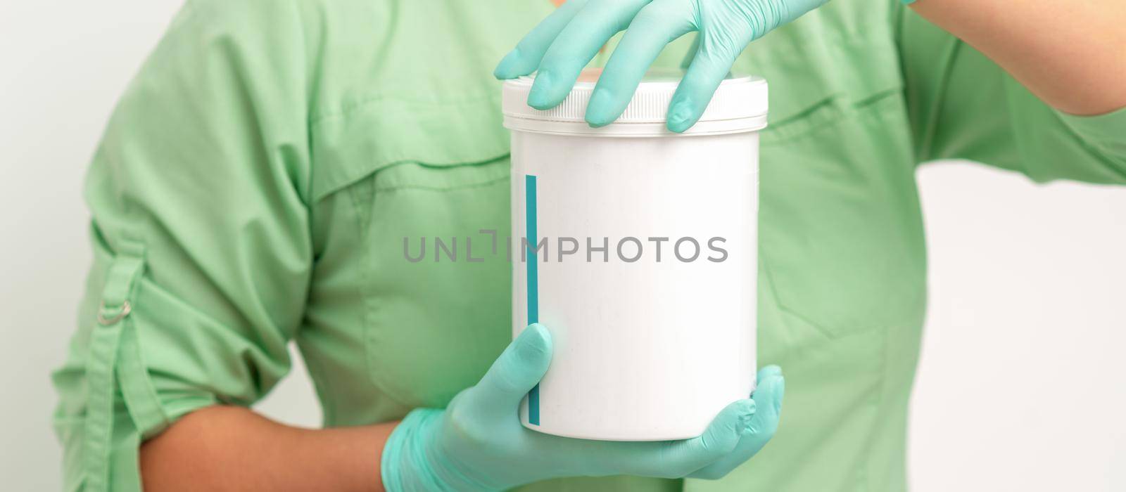 Hands in protective gloves of beautician open a white body cream jar on white background