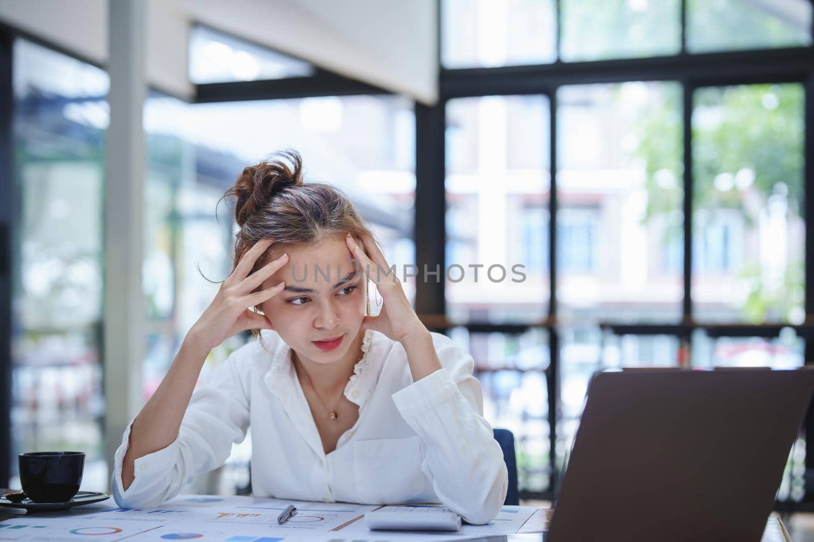 A portrait of a young employee showing an anxious and stressed face from working on paperwork on a desk.