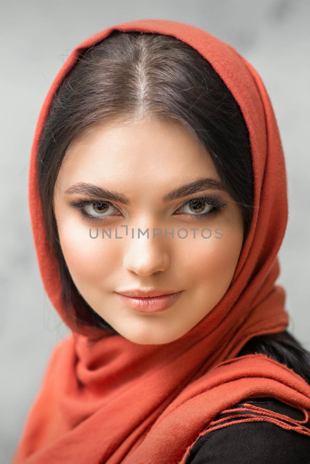 Portrait of a pretty young caucasian woman with makeup in a red headscarf on gray background