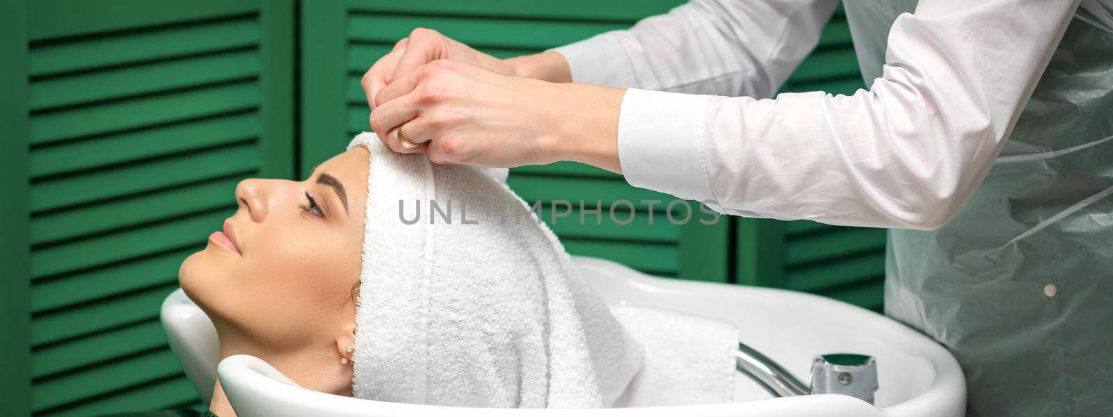 A hairdresser is wrapping a female head in a towel after washing hair in the beauty salon. by okskukuruza