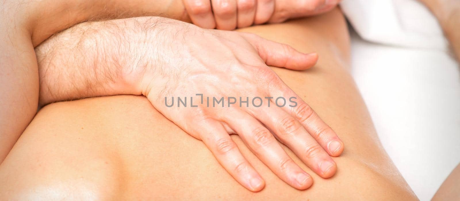 A male physiotherapist stretches the arms on the back of a man lying down, close up