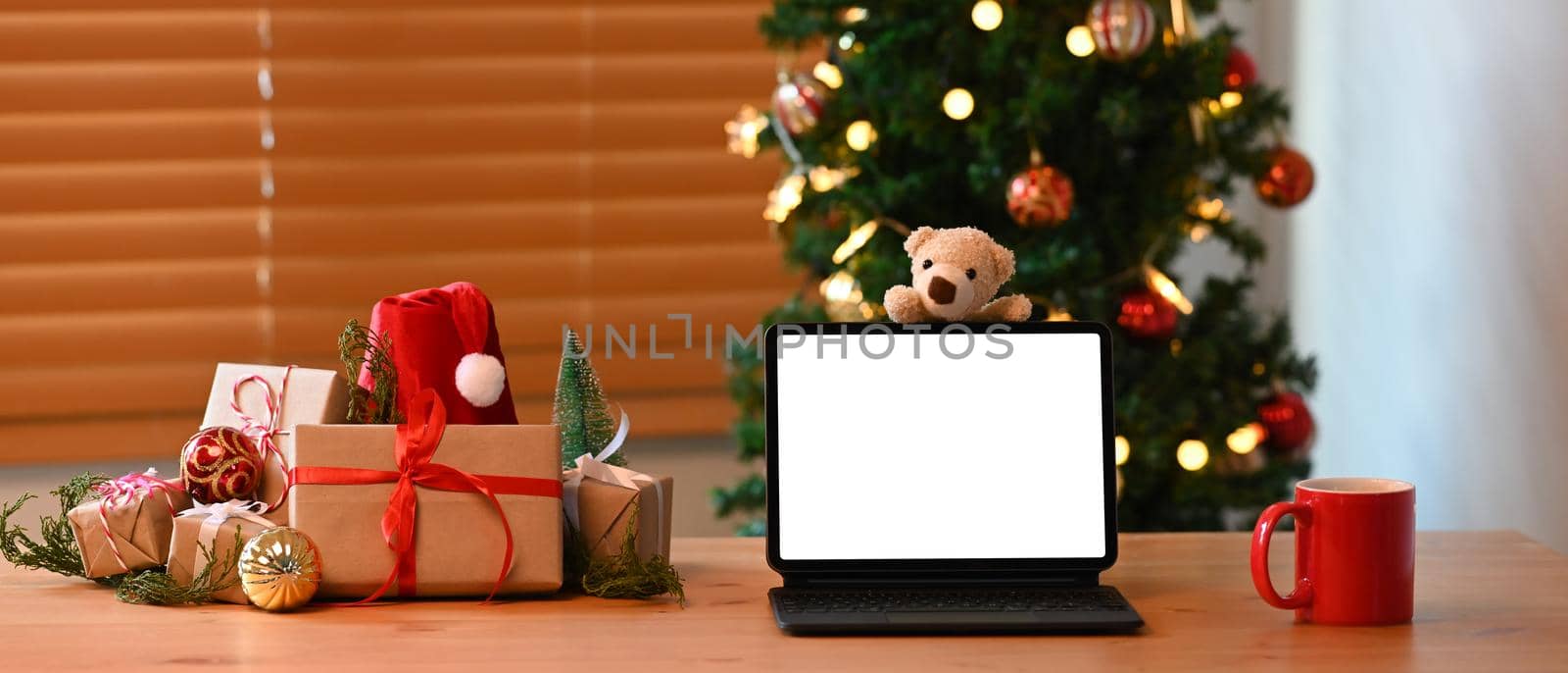 Computer tablet, cup of hot beverage and Christmas gift boxes on wooden table.