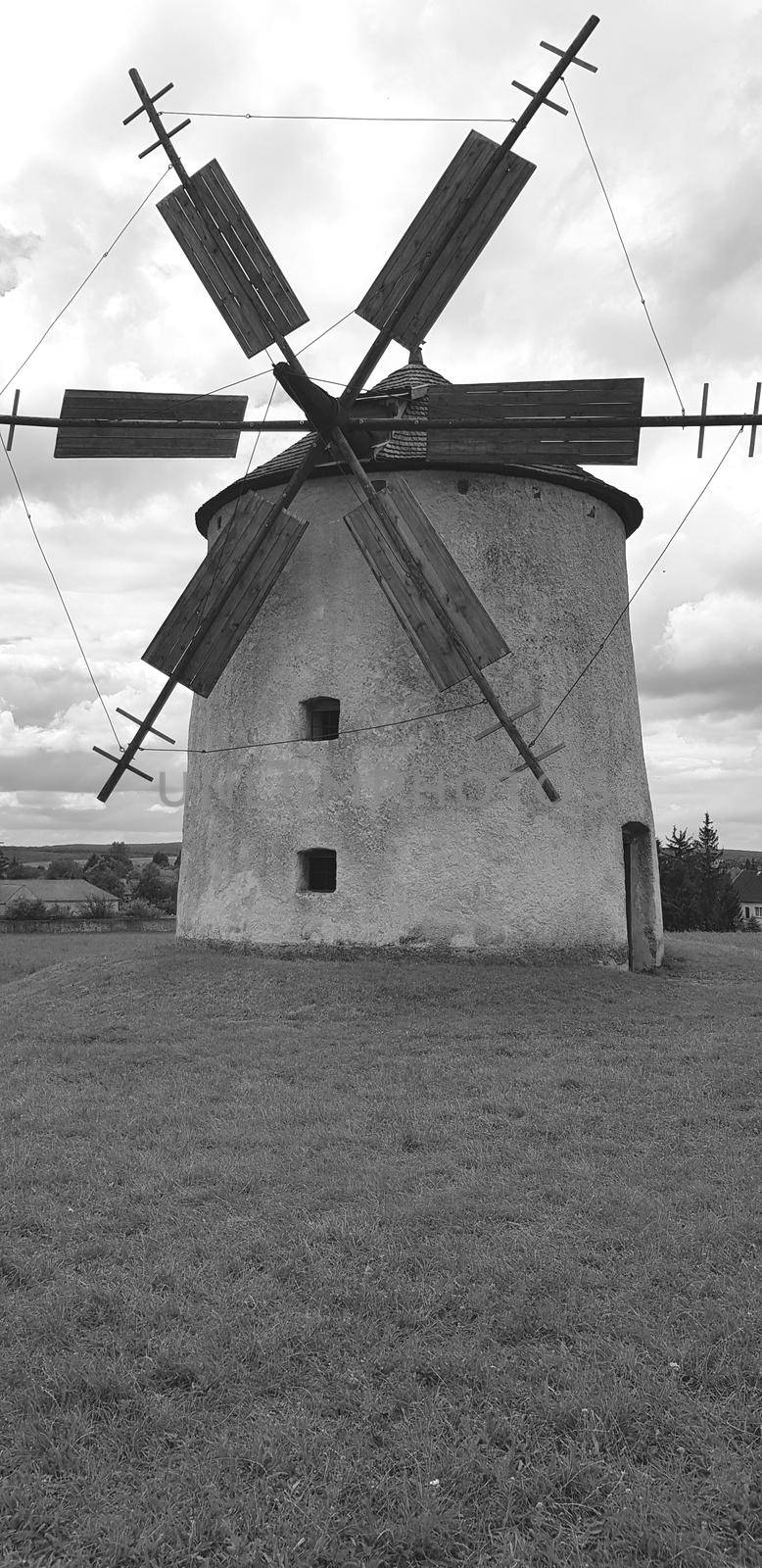 Black and white photo with an old windmill sitting in a field with a cloudy sky by banate