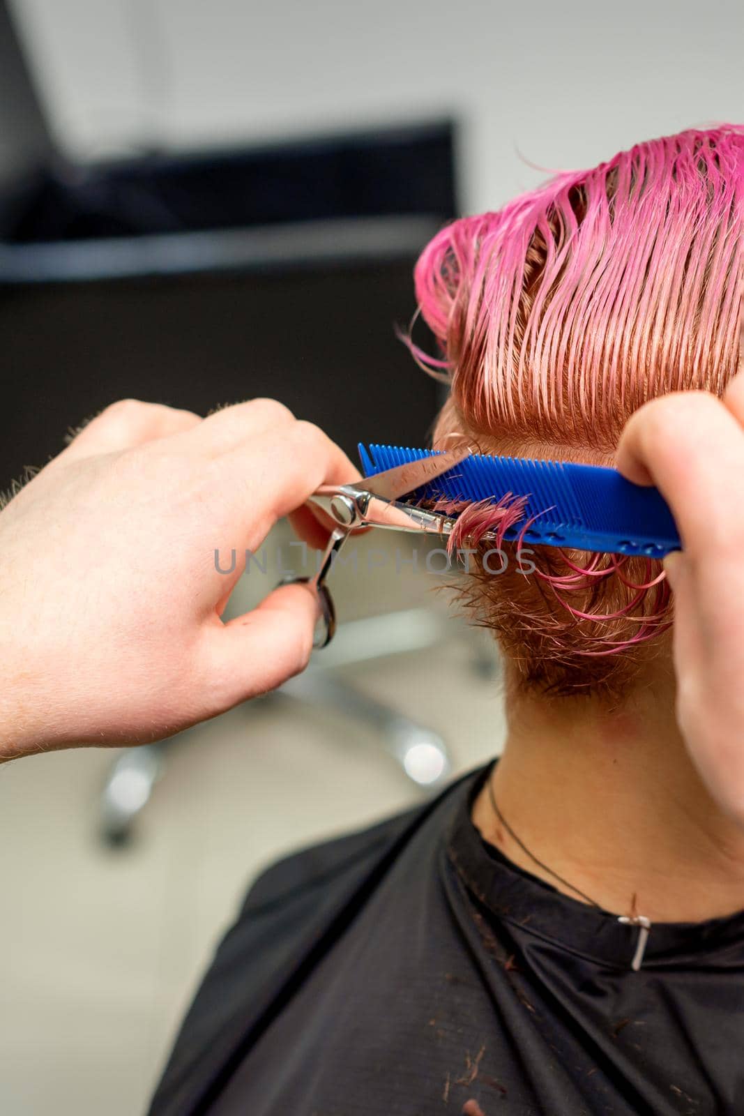 Hairdresser cuts dyed wet pink short hair of young caucasian woman combing with a comb in a hair salon. by okskukuruza