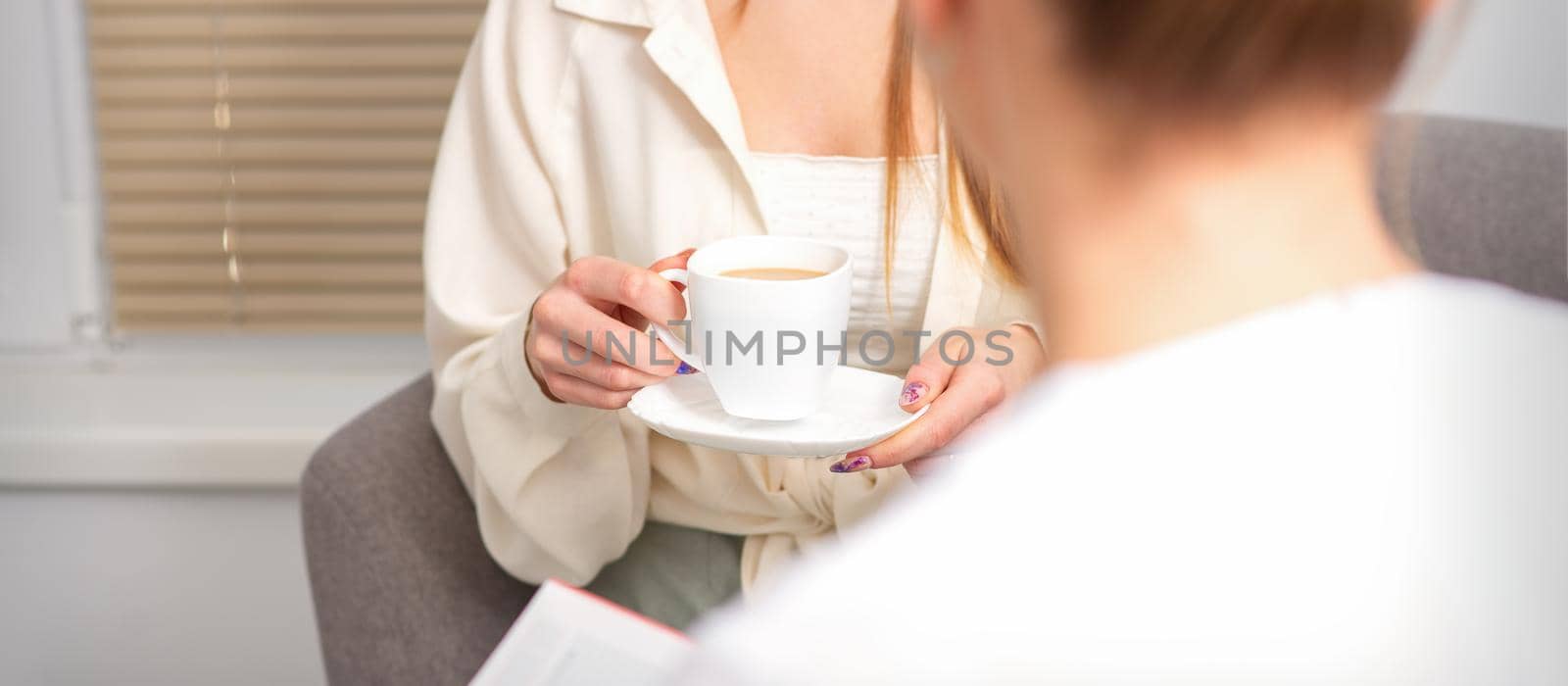 The young caucasian woman has a coffee and appointment with a female doctor in hospital office