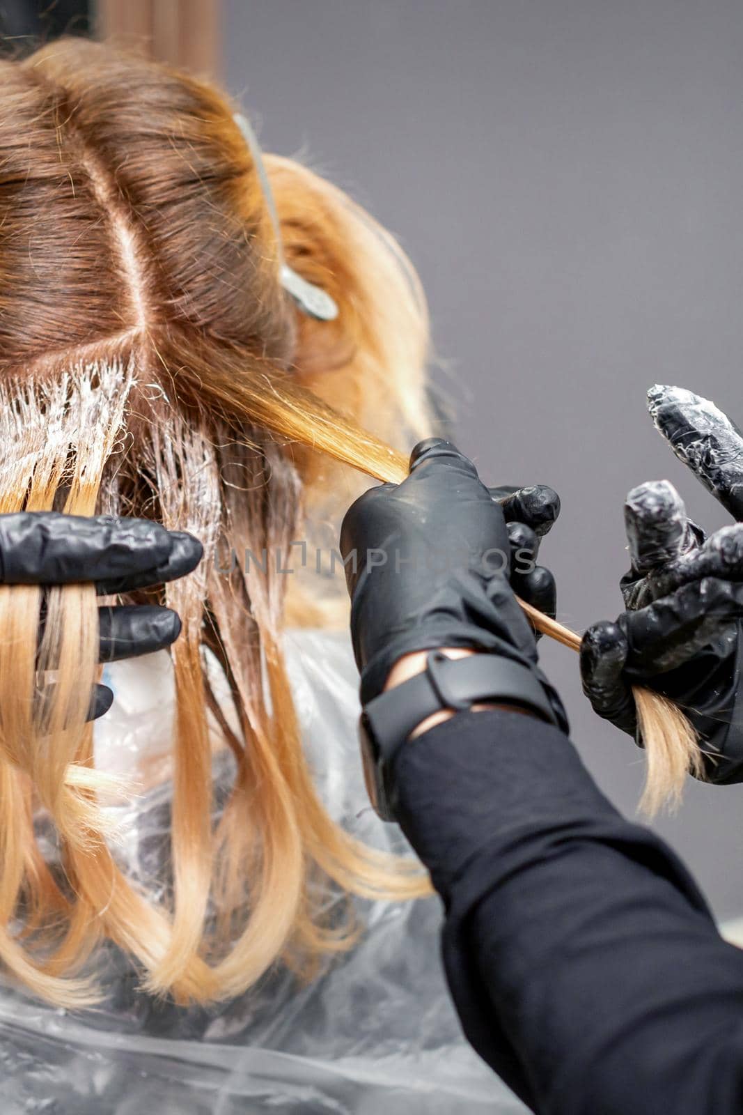 A hairdresser is applying color to hair in black gloves. Hair coloring in a beauty salon. Beauty concept. by okskukuruza