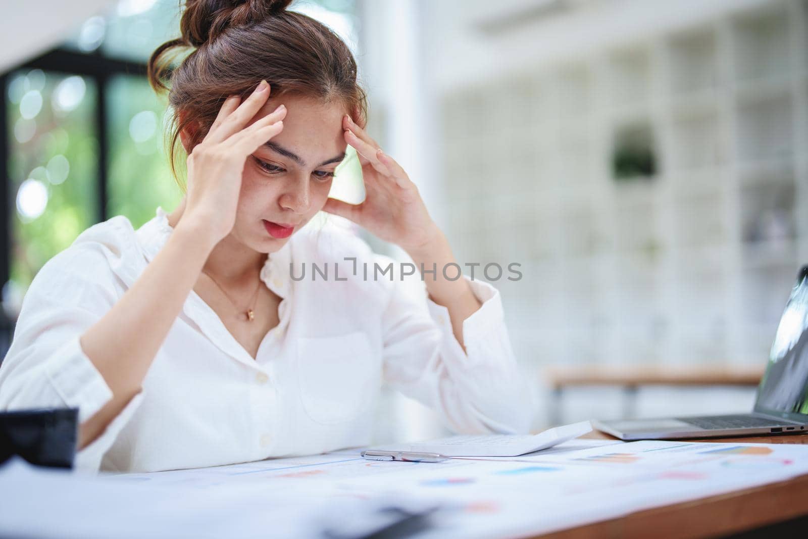 A portrait of a young employee showing an anxious and stressed face from working on paperwork on a desk.