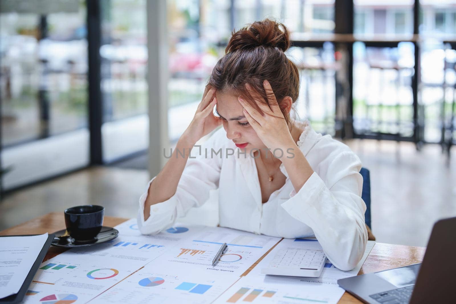 A portrait of a young employee showing an anxious and stressed face from working on paperwork on a desk.