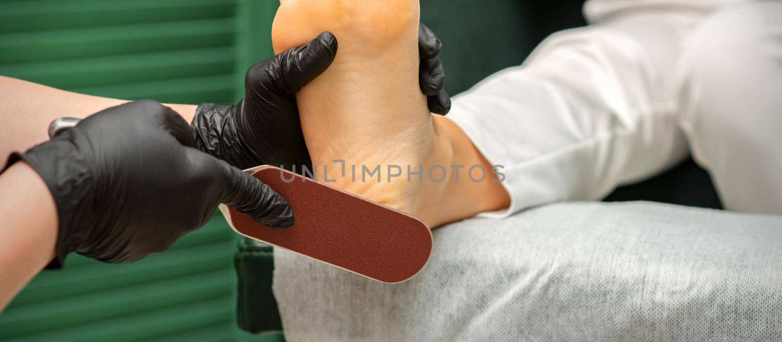 Peeling of Heels. Hands of pedicure master scrape dead from heel skin by special grater in spa salon. by okskukuruza